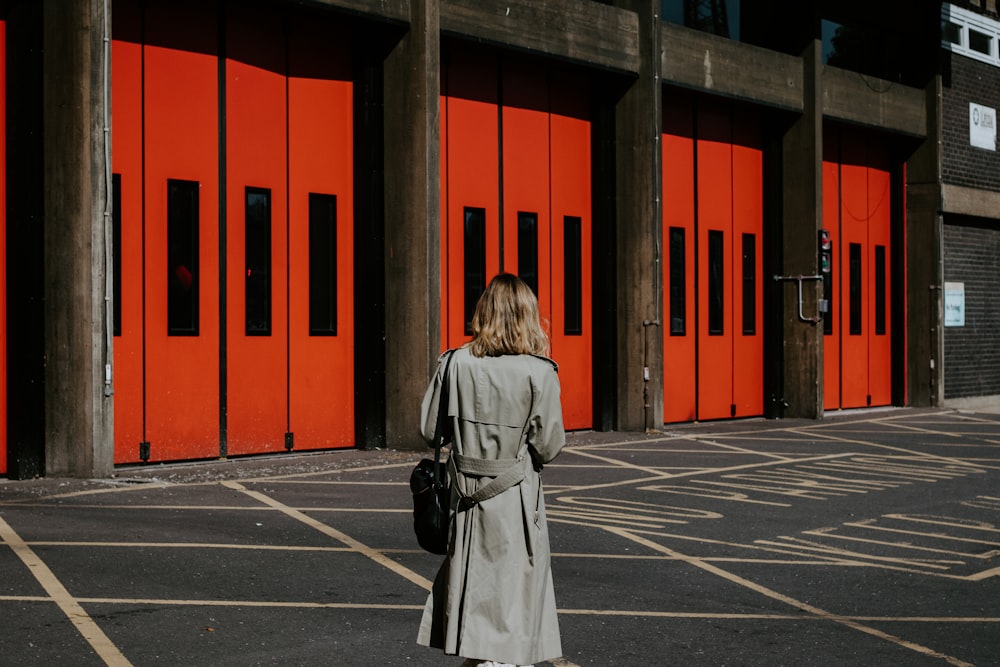 woman in brown coat standing near red building during daytime