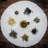 An assortment of various dried tea leaves and blossoms is arranged on a circular white cloth placed on a wooden surface. The teas include dark loose leaf piles, a small group of yellow blossoms, and a round citrus shell filled with tea leaves.
