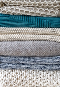 Stack of neatly folded hand-knitted sweaters in earthy tones on a wooden table
