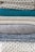 A stack of neatly folded knitted sweaters showcasing a variety of textures and patterns. The pile features different knit designs, including a honeycomb pattern and ribbed styles, in neutral tones with one teal garment in the middle.