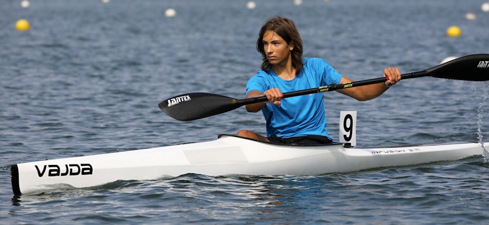 woman in red and blue plaid shirt riding white kayak on water during daytime