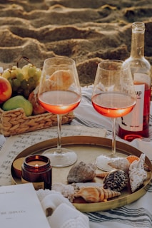 A cozy beach picnic setup with a soft blanket, sunglasses, and a sunshell bag beside a sparkling ocean
