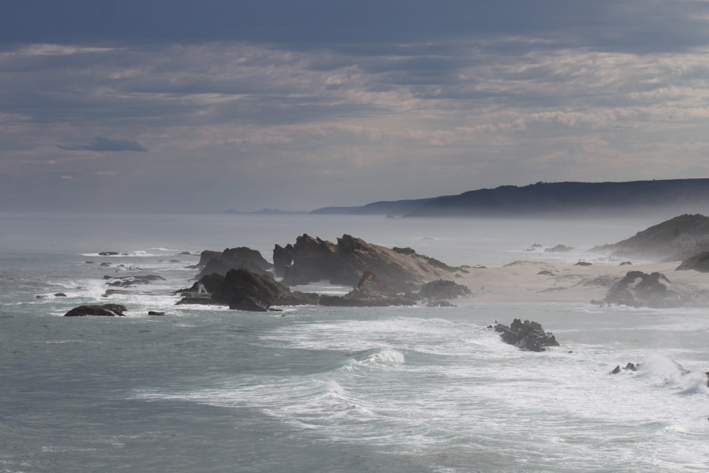 brown rock formation on sea under white clouds and blue sky during daytime