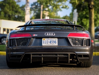 A sleek, black sports car is parked on the road. It features distinctive red taillights, a Virginia license plate, and a visible Audi R8 badge. The vehicle is surrounded by an outdoor setting with trees and a blurred background.