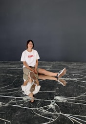 woman in white t-shirt and brown skirt sitting on gray concrete floor