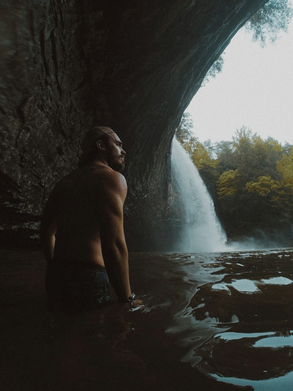 topless man in black shorts standing in cave