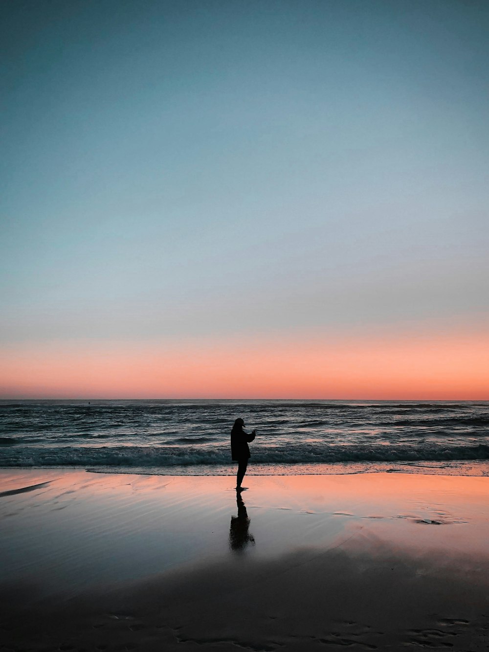 夕暮れ時の浜辺を歩く人のシルエット