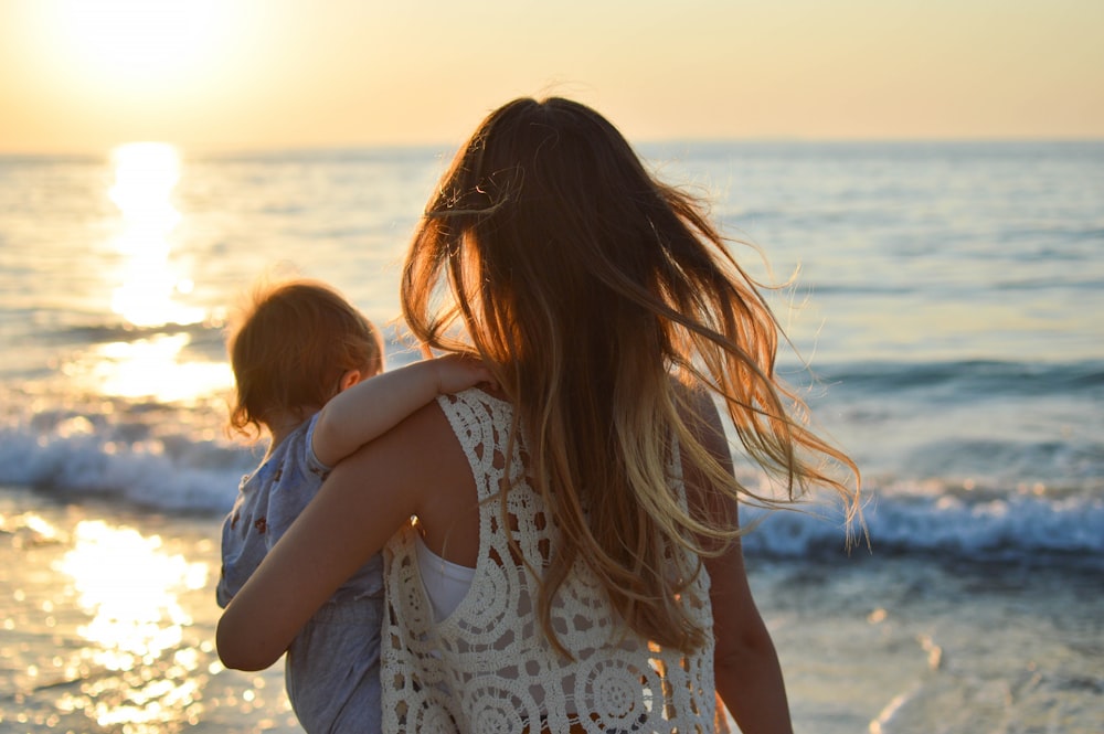 woman in white tank top carrying child in blue shirt