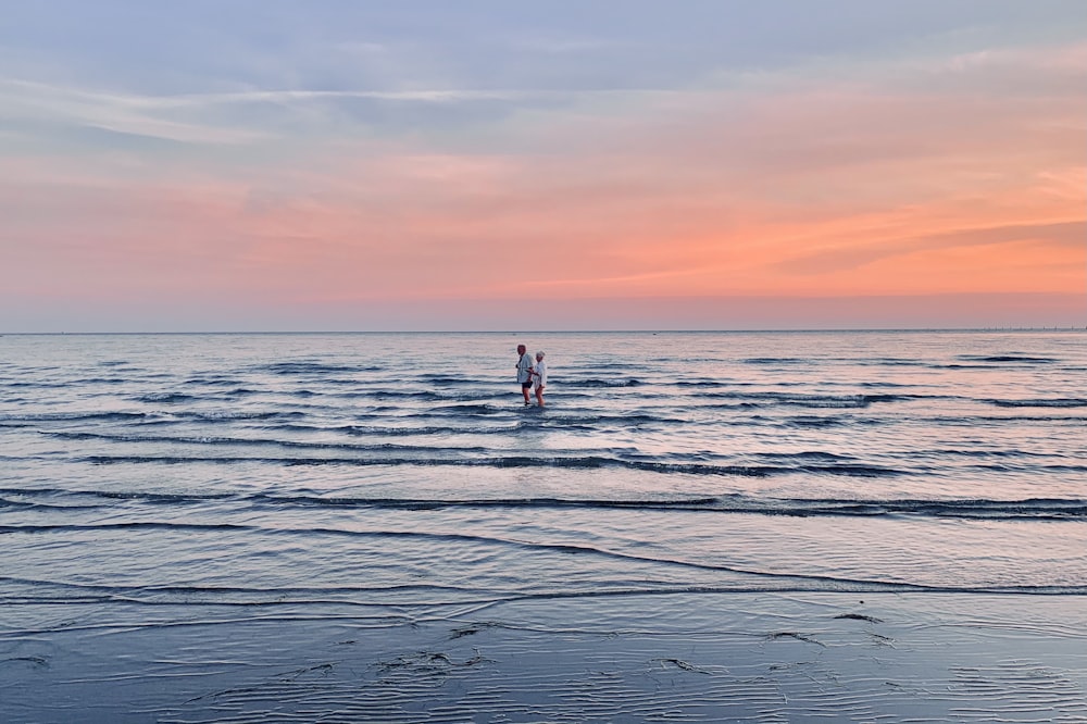 2 person standing on sea shore during sunset