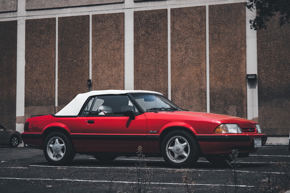 red and white coupe parked beside brown concrete building during daytime