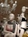Two mannequins are displayed in a retail store setting. One wears a pink bra with a black and white patterned scarf, while the other is dressed in a black bikini and a floral-patterned jacket. Overhead, an ornate chandelier with dangling crystals is illuminated. The background shows a store environment with various clothing items visible on racks.
