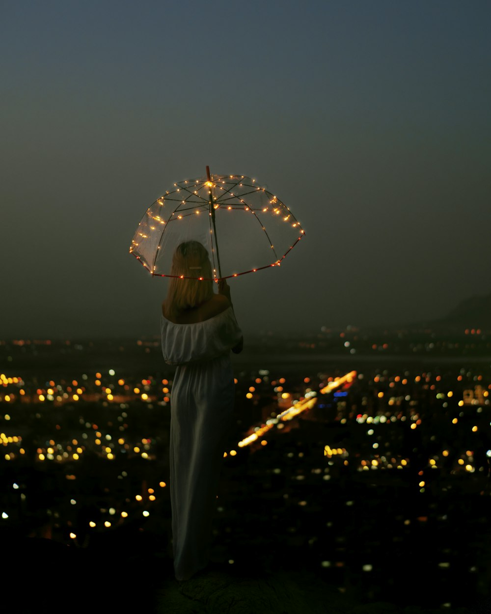 Femme en robe blanche tenant un parapluie pendant la nuit