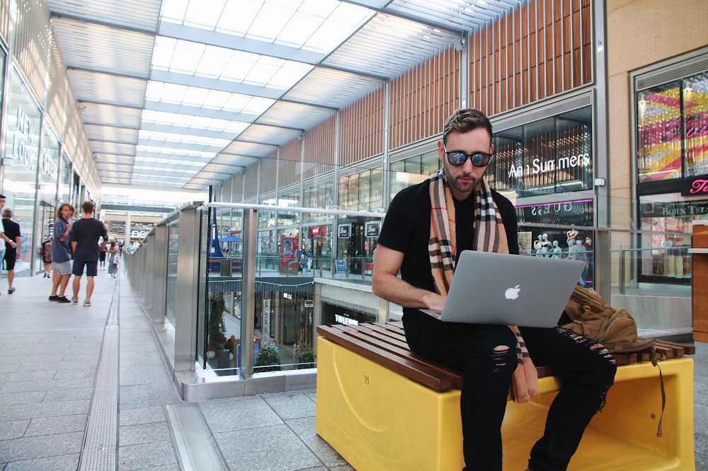 Frau in schwarzem Hemd und gelber Hose mit silbernem MacBook