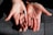 Two open hands are positioned side by side against a textured surface. A small hearing aid rests in one palm. The hands are adorned with rings and a bracelet, and the skin is illuminated by natural light, highlighting their texture.