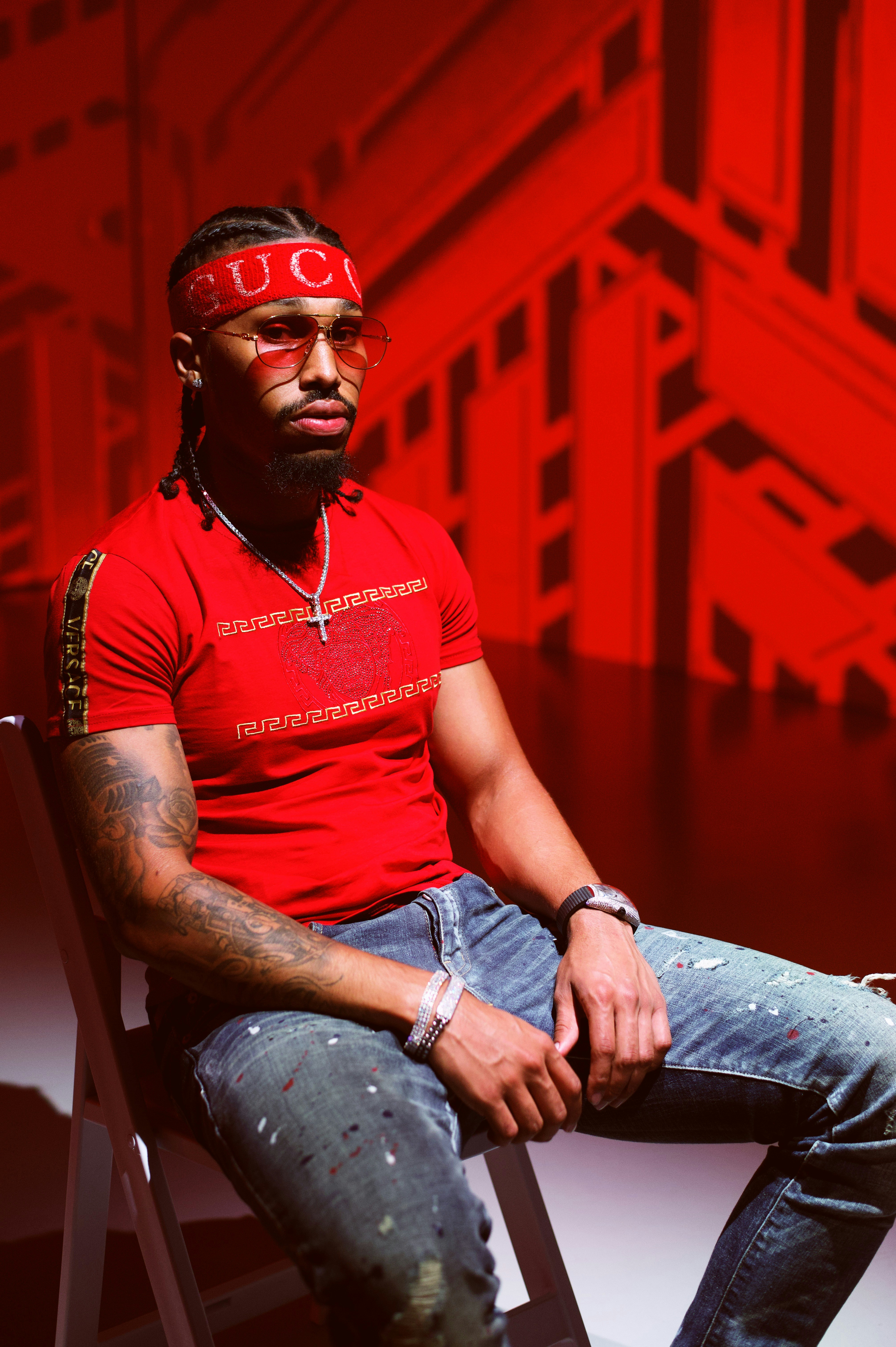 man in red crew neck t-shirt and blue denim jeans sitting on chair