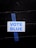 A white sign with the words 'VOTE BLUE' in blue capital letters is taped to a black brick wall using a piece of blue painter's tape.