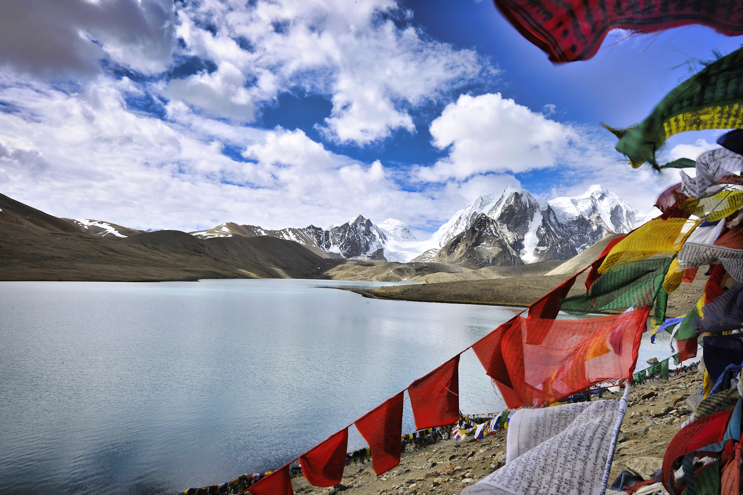 Prayer flags on a high-altitude lake shore beneath snow peaks, North Sikkim