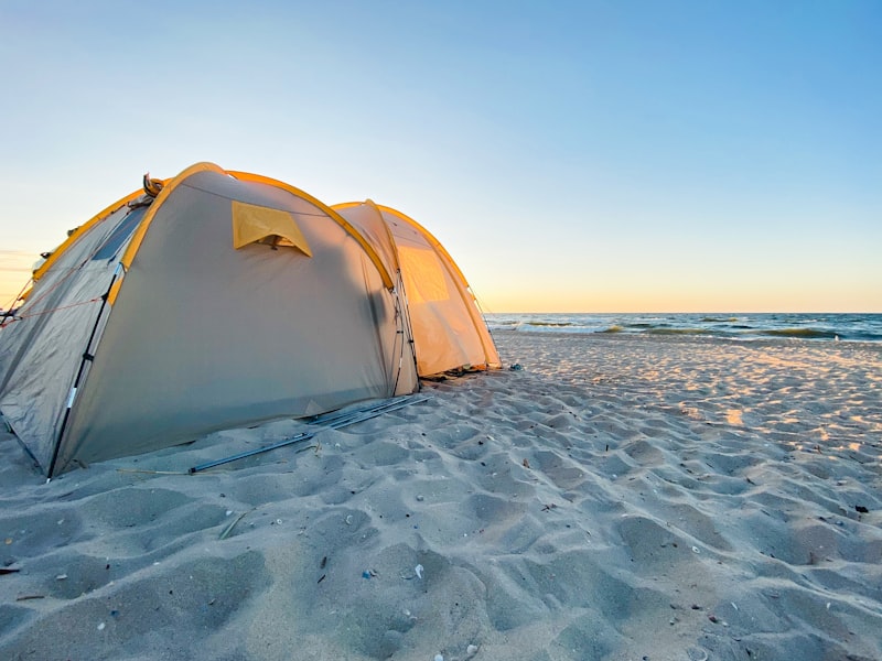 Tenda putih di pasir pantai saat siang, persiapan camping di pantai yang aman