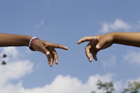 Two hands are reaching towards each other against a clear blue sky. One hand is wearing a black bracelet with the words 'MATTER' visible. The scene resembles a famous artistic representation of human connection.