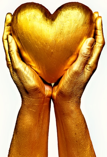 persons golden hands holding a golden heart