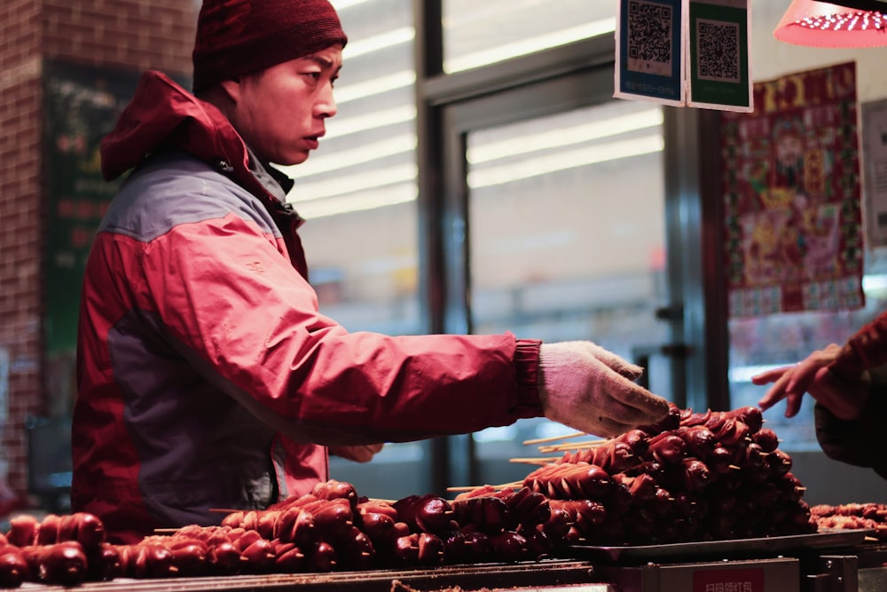 man in pink jacket and red knit cap holding red fruit