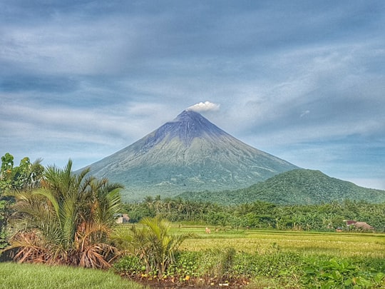 green grass field near mountain under white clouds and blue sky during daytime in Mayon Volcano Philippines
