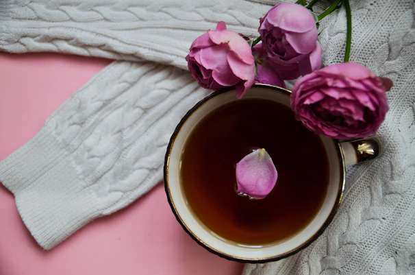 A cozy flat lay of a warm beige sweater, delicate gold jewelry, and a cup of herbal tea.