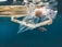 Underwater scene with a piece of plastic debris floating among small striped fish. The water is a deep blue, and the presence of the plastic creates an unsettling contrast with the natural marine life.