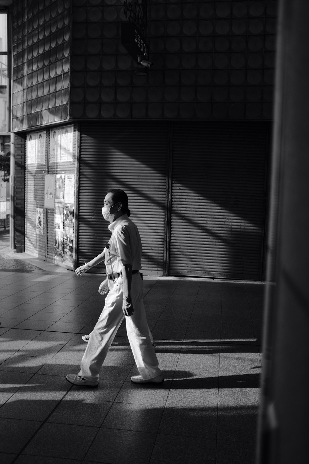 grayscale photo of man in white jacket and pants walking on sidewalk