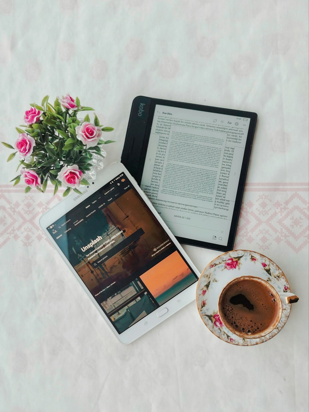 black ipad beside white ceramic mug on white and pink floral table cloth