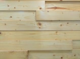 Several overlapping wooden planks with visible grain patterns and knots. The wood has a smooth finish and light natural color.