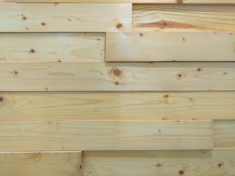 Several overlapping wooden planks with visible grain patterns and knots. The wood has a smooth finish and light natural color.