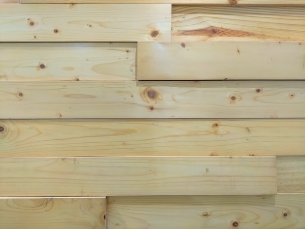 Several overlapping wooden planks with visible grain patterns and knots. The wood has a smooth finish and light natural color.