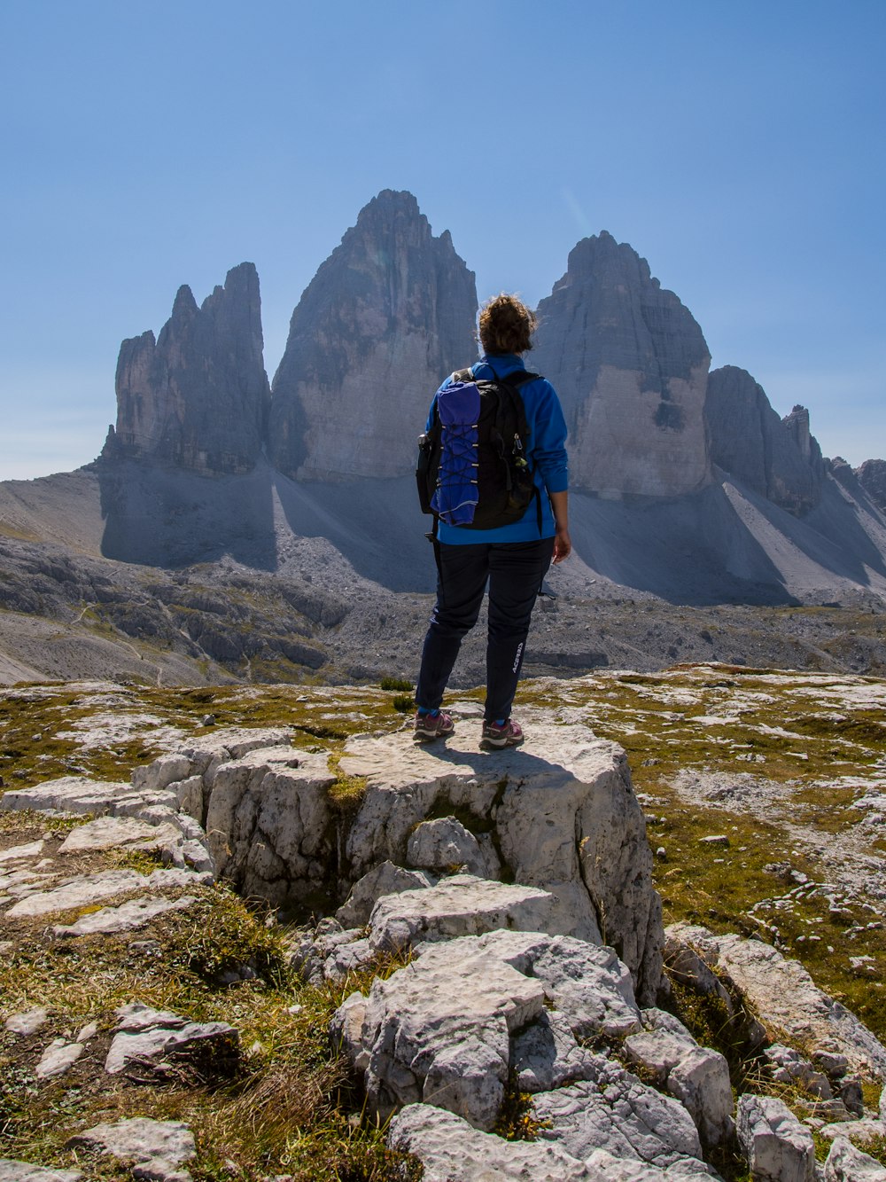 man in blue jacket and black pants standing on rock formation during daytime