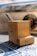 A wooden pencil holder with two pens inside is placed on a surface that appears to have blueprints or technical drawings. The pencil holder has the word 'RAUCH' printed on it. In the background, there's a blurred circular object with colorful elements.