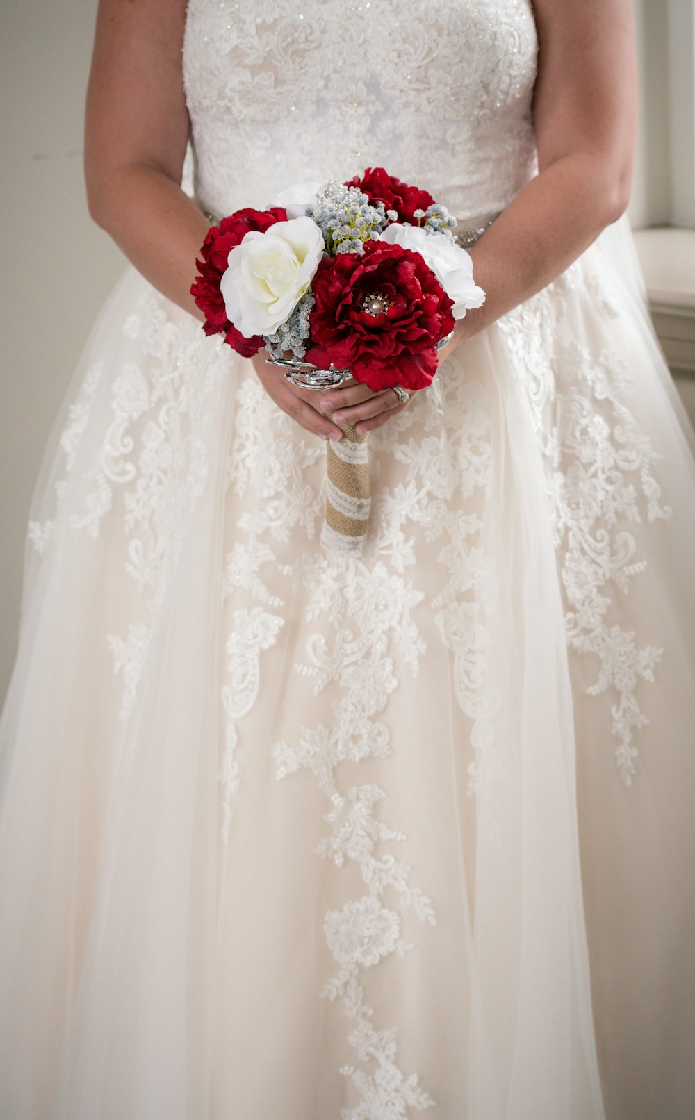 woman in white floral wedding dress holding bouquet of red and white roses