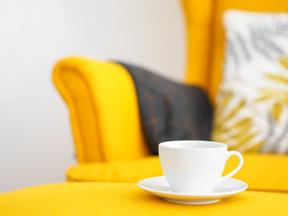 white ceramic cup on white ceramic saucer on yellow sofa