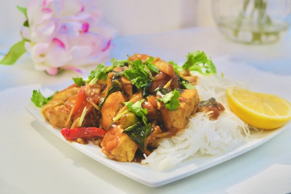 A vibrant plate of chili chicken garnished with green chilies and spring onions.