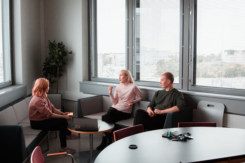 2 women and a man sitting on grey sofas having a conversation