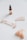 A flatlay featuring a jade roller with rose gold accents, a small gua sha tool, an amber-colored dropper bottle with a label, and several rose quartz stones. They are arranged on a white background, creating a minimalistic and clean aesthetic.