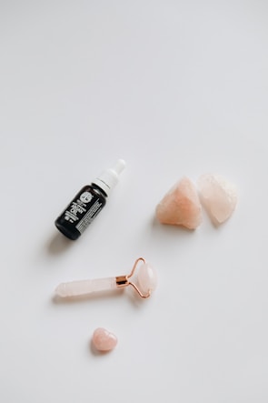 Close-up of hands holding a delicate rose quartz facial roller on a marble countertop.