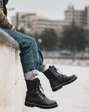 person in blue denim jeans and black leather shoes sitting on concrete wall during daytime
