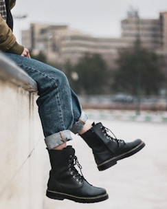 person in blue denim jeans and black leather shoes sitting on concrete wall during daytime