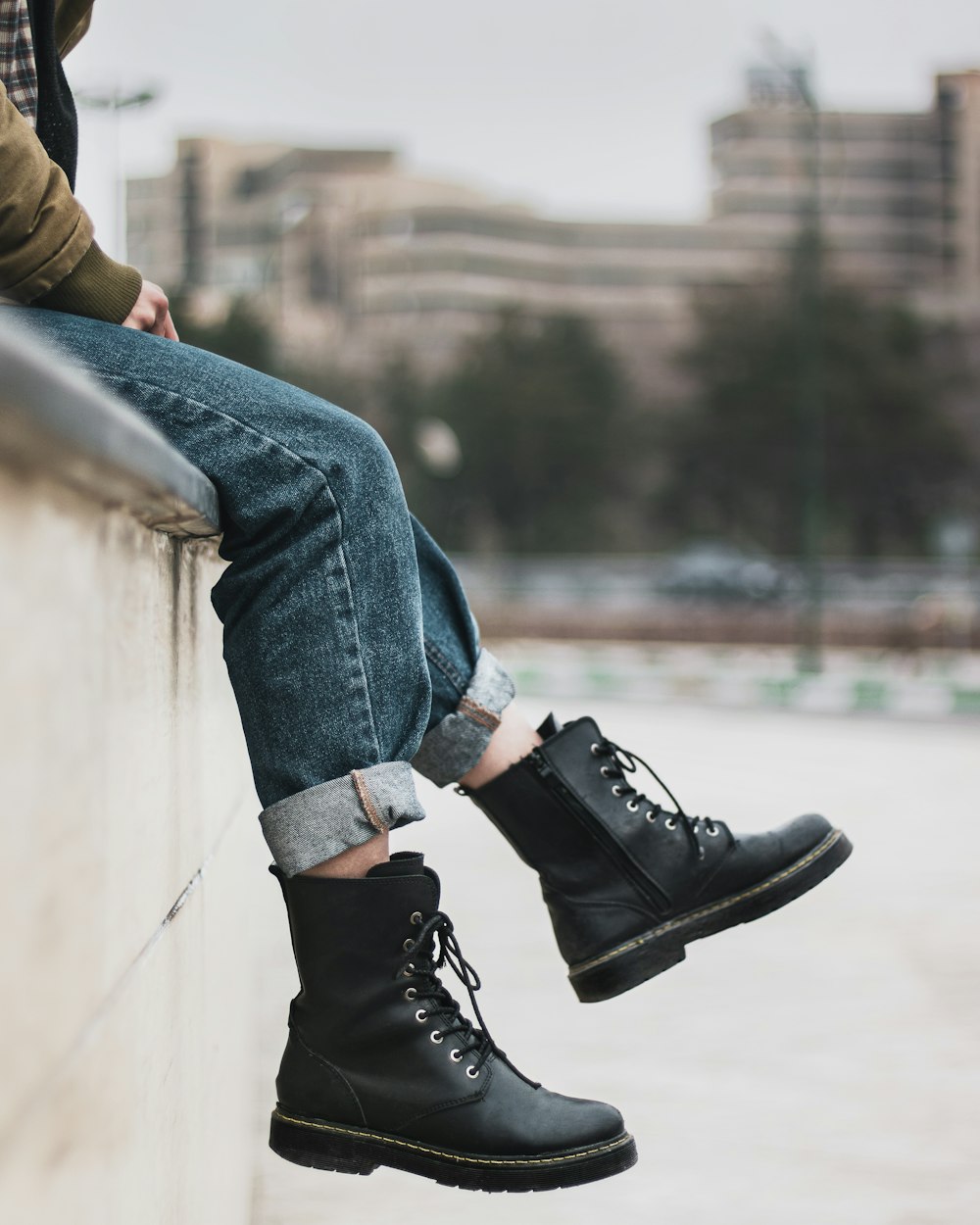 昼間、コンクリートの壁に座っているブルーデニムのジーンズと黒い革靴を履いた人