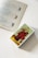 A tarot card deck is placed on a white surface next to an open book with descriptions and illustrations of various tarot cards. The top card on the deck displays the Three of Cups card depicting three women in red robes holding golden cups.