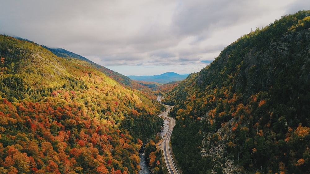 gray concrete road between green and brown mountains under white cloudy sky during daytime