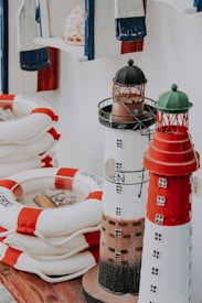 The image features several items with a nautical theme, including model lighthouses and stacked lifebuoys in white and red. The background contains blue and white decorations and a seashell.