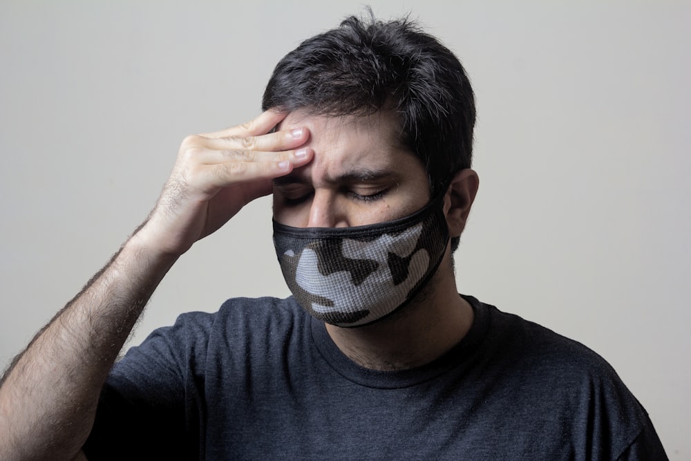 homme en chemise noire à col rond couvrant son visage avec un textile noir et blanc