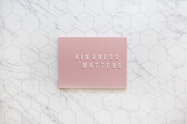 A pink pegboard with the words 'KINDNESS MATTERS' in white letters placed on a hexagonal tiled surface with a marble pattern.