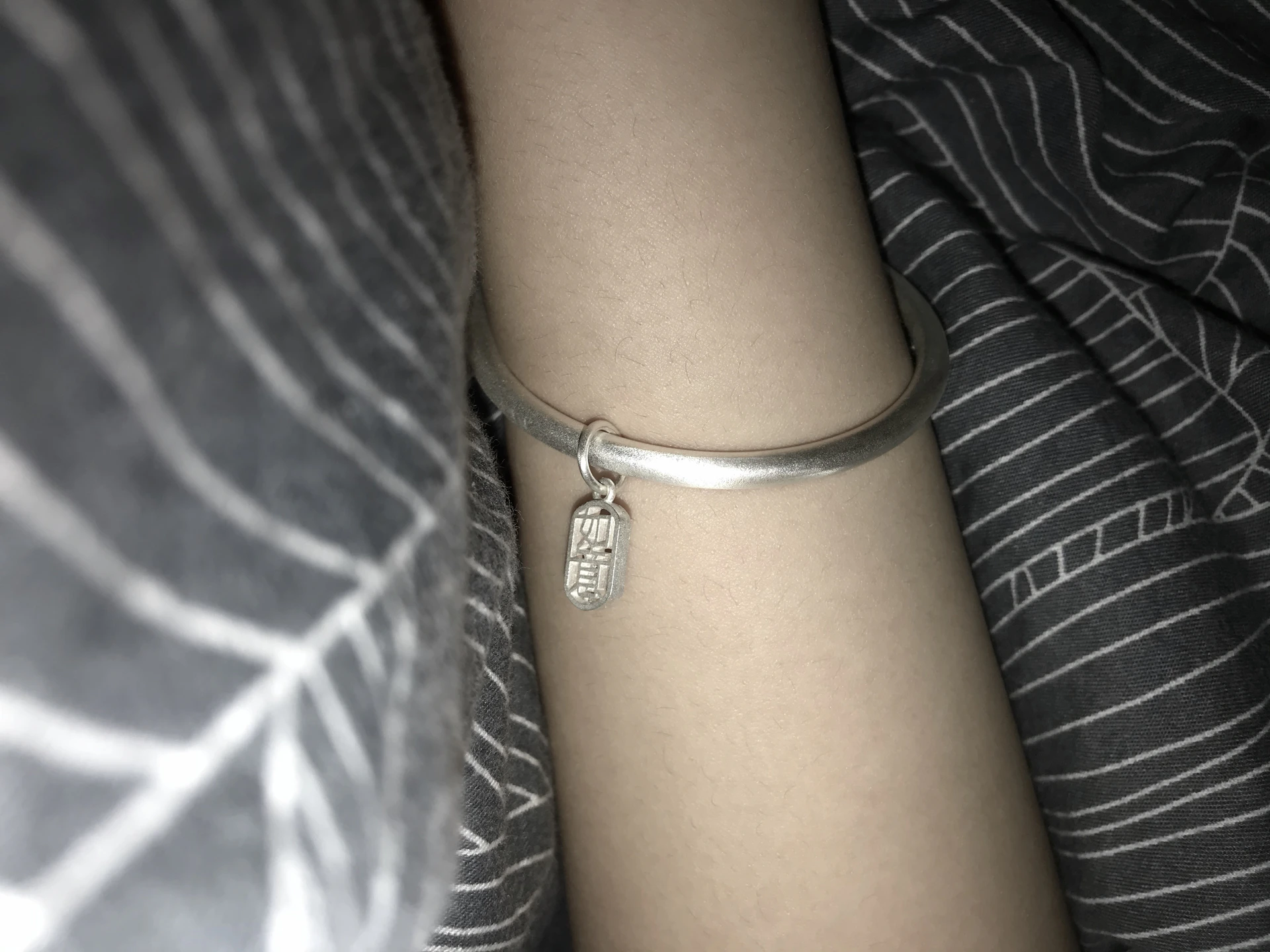 A stylish silver bracelet wrapped around a wrist, set against a backdrop of soft fabric in warm tones.